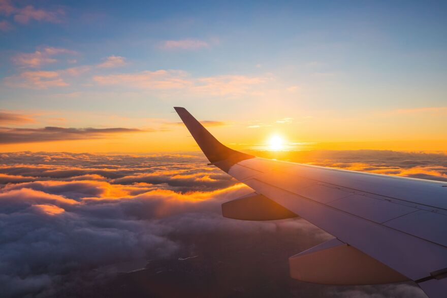 Airplane flight in sunset sky over ocean water and wing of plane